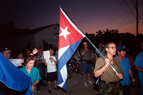 Cuban protestors, with one man in the front holding up the Cuban flag. 